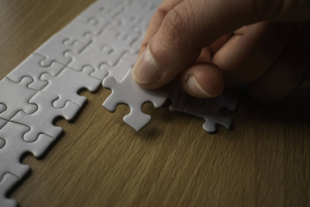 Крупним планом рука наносить інший шматок на білий шматок головоломки на дерев'яний стіл
 - Фото, зображення