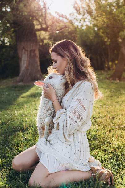 Junge Frau mit Schafen auf dem Feld. Mädchen sitzt auf Gras und umarmt kleine Schafe - Foto, Bild