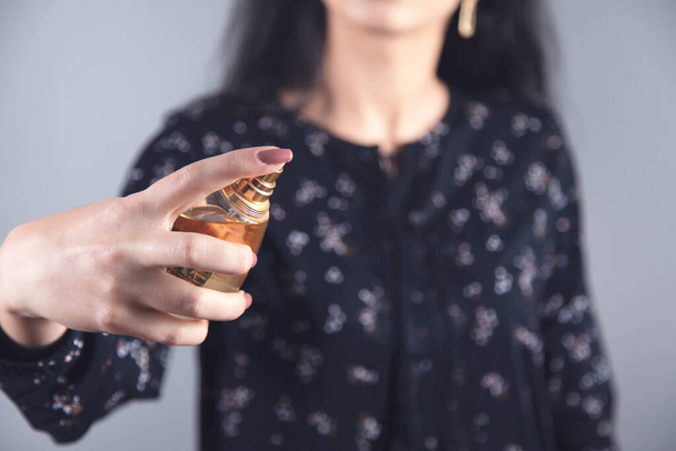 woman hand holding bottle of perfume on grey background - Zdjęcie, obraz