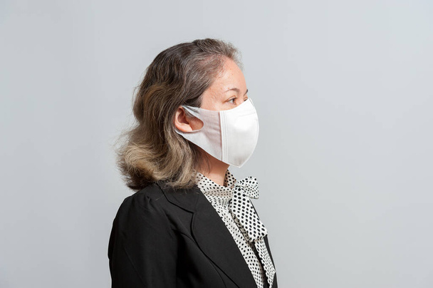 Zijaanzicht van middelbare leeftijd gemengde ras vrouw in formele dragen witte chirurgische masker ter bescherming tegen coronavirus (COVID-19). Geïsoleerd op witte achtergrond. Zijaanzicht. - Foto, afbeelding