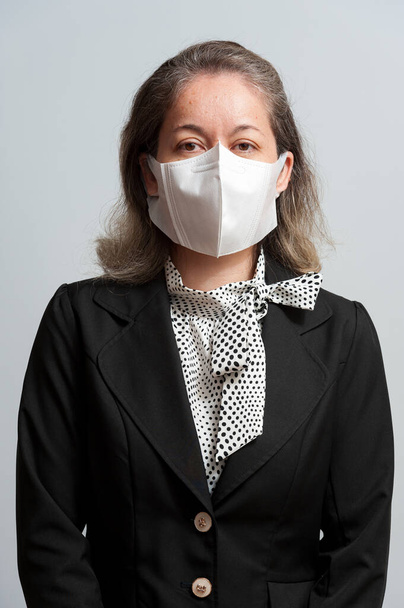 Vista lateral de una mujer mestiza de mediana edad vestida formalmente con máscara quirúrgica blanca para protegerse contra el coronavirus (COVID-19). Aislado sobre fondo blanco. Vista lateral
. - Foto, imagen