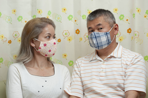 Coppia di mezza età che indossa maschera facciale in tessuto fai da te per la protezione contro il coronavirus (COVID-19) e altre malattie infettive. sfondo tenda floreale
. - Foto, immagini