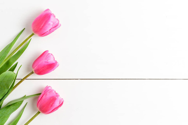 Vue latérale de trois petites fleurs rose vif de tulipe et feuilles vertes sur une table en bois peint en blanc, beau fond floral intérieur photographié avec un petit focus
 - Photo, image