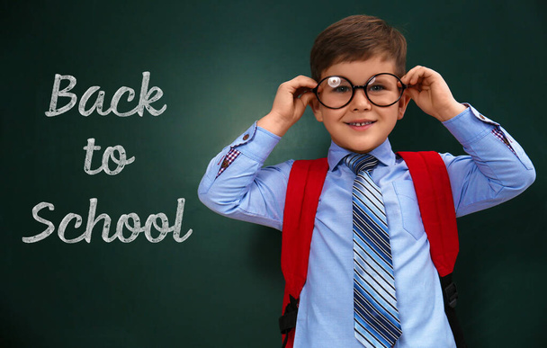 Cute little child wearing glasses near chalkboard with phrase BACK TO SCHOOL - Foto, afbeelding