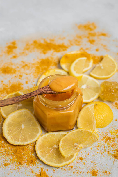 Flower honey in a jar, lemons and turmeric on a light background. Alternative medicine concept. Super food. - Fotó, kép