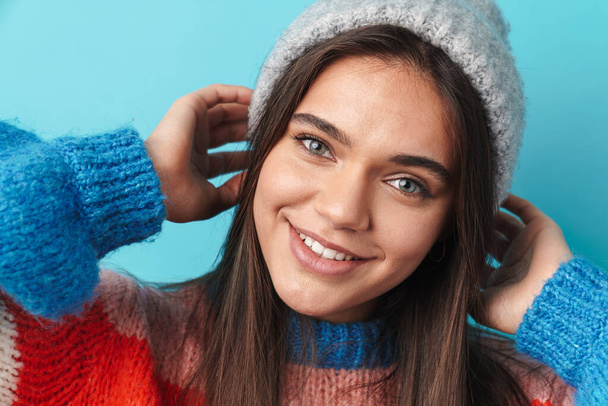 Image of happy beautiful woman in knit cap smiling and looking at camera isolated over blue background - 写真・画像