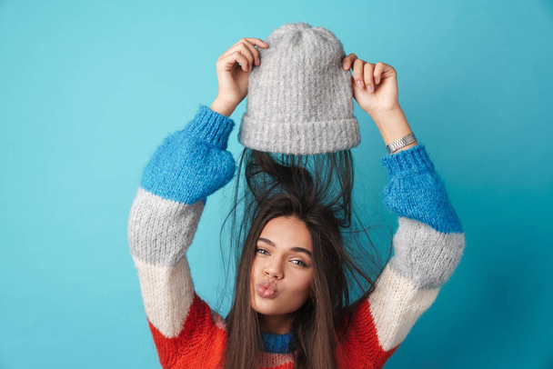 Image of happy beautiful woman making kiss lips and fun with knit cap isolated over blue background - Fotoğraf, Görsel