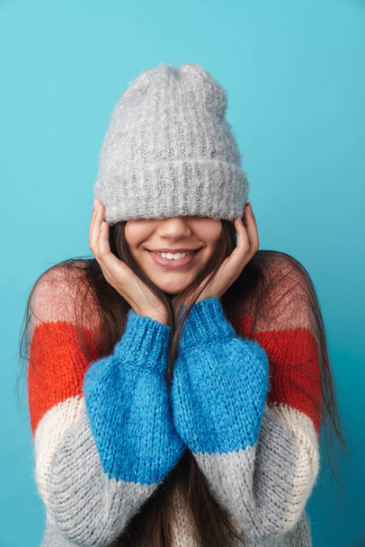 Image of a young positive smiling woman posing isolated over blue wall background covering face with hat. - Фото, зображення
