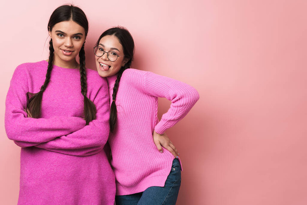 Image of two happy teenage girls with braids in casual clothes smiling at camera isolated over pink background - Foto, immagini