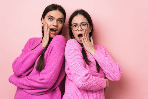 Two cheerful cute teenage girls standing back to back isolated over pink background - Valokuva, kuva