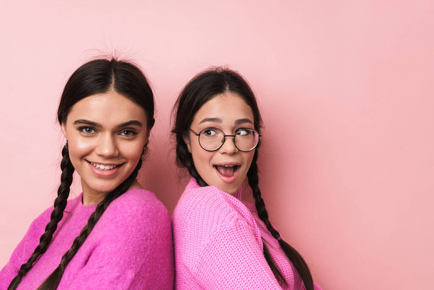 Image of two happy teenage girls with braids in casual clothes smiling at camera isolated over pink background - Fotografie, Obrázek