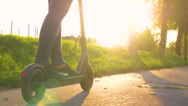 LOW ANGLE: Cinematic shot van een vrouw in jeans rijden een e-scooter bij zonsondergang. - Video