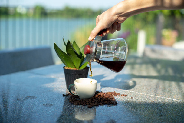 Hand of barista pouring the coffee from the glass jar into the cup at the outdoor garden - Photo, Image