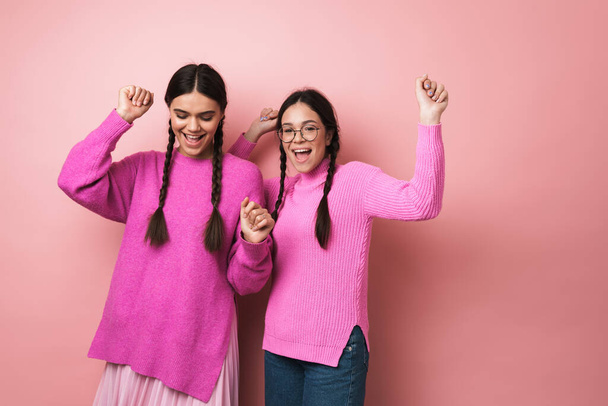 Two cheerful cute teenage girls dancing isolated over pink background, having fun - Foto, afbeelding