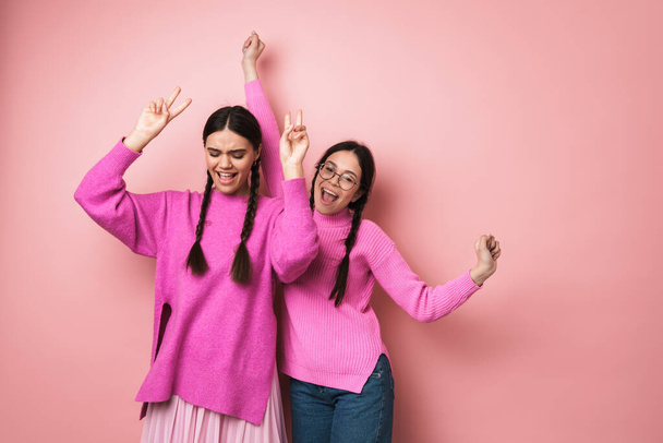 Two cheerful cute teenage girls dancing isolated over pink background, having fun - Photo, image
