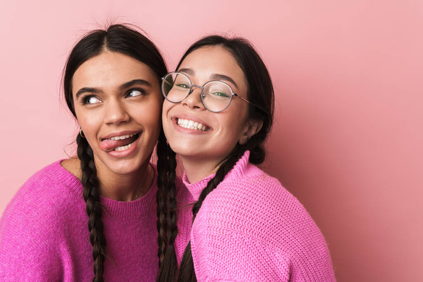 Two cheerful cute teenage girls having fun isolated over pink background, grimacing - Photo, image