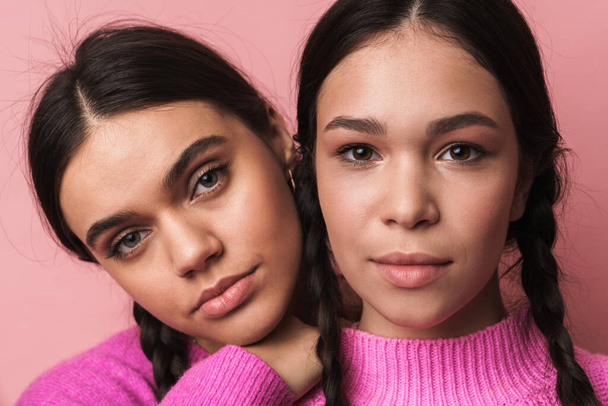 Image of two attractive teenage girls with braids in casual clothes looking at camera isolated over pink background - Valokuva, kuva