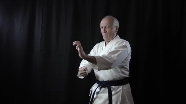Formální cvičení karate jsou trénovány starým mužským atletem na černém pozadí - Záběry, video