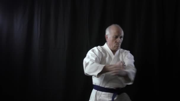Blocks and punches an old man athlete arms is training on a black background - Footage, Video