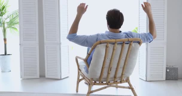 Calm young man relaxing in comfortable wooden chair enjoying lounge - Кадри, відео