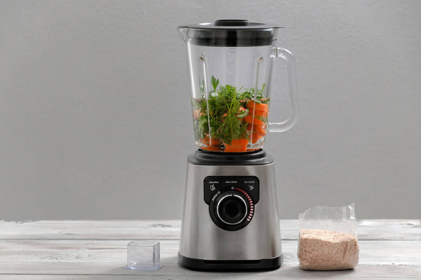 Blender, carrot, parsley, dill on a gray wooden table. Girl makes a smoothie of vegetables. Healthy lifestyle. Dietary nutrition. Carrots and greens close-up. - Photo, Image