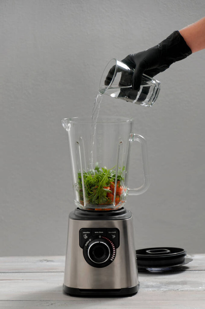 Blender, carrot, parsley, dill on a gray wooden table. Girl makes a smoothie of vegetables. Healthy lifestyle. Dietary nutrition. Carrots and greens close-up. - Photo, Image