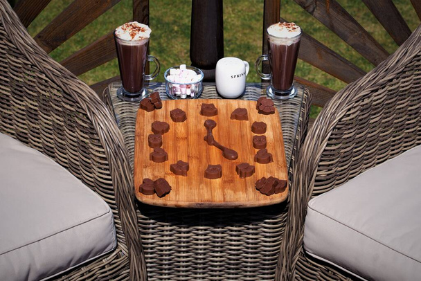 Capturing a clock created from home made chocolates and two chocolate spoons, in front of two hot chocolate drinks, served with sprinkles and marshmallows. - Photo, Image