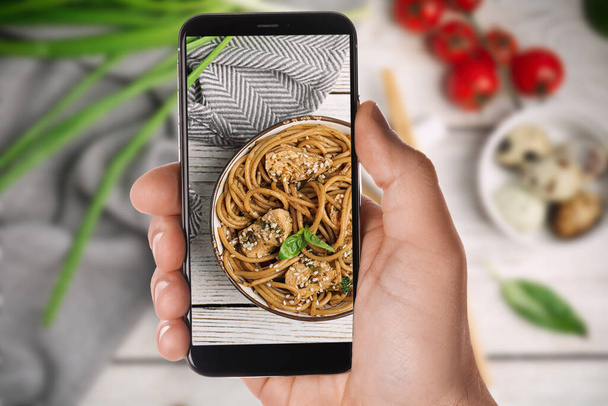 Blogger taking picture of delicious buckwheat noodles with meat at table, closeup. Food photography - Fotó, kép