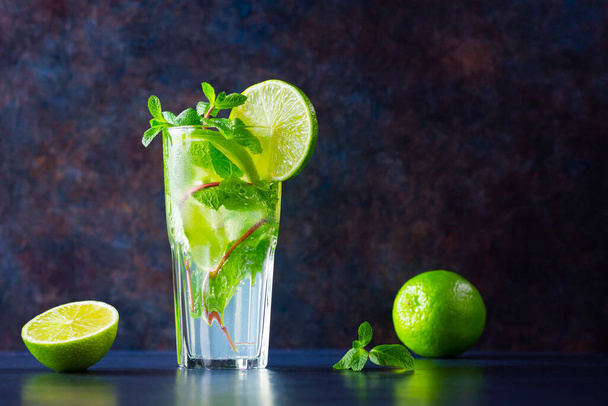 Mojito cocktail with lime and mint in tall glass. Fresh mojito in glass on a dark background. Refreshing mint cocktail with lime. Infused water - Φωτογραφία, εικόνα