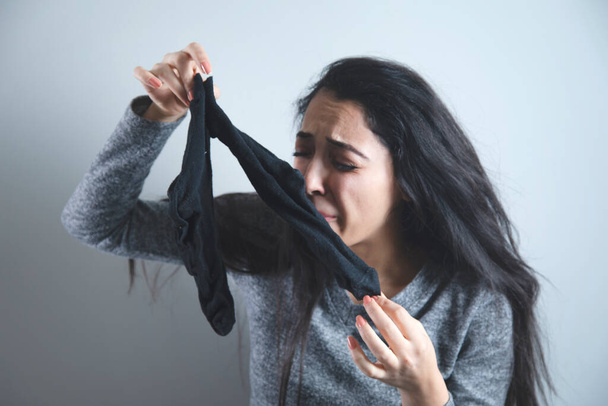 woman smell of socks on grey background - Foto, afbeelding