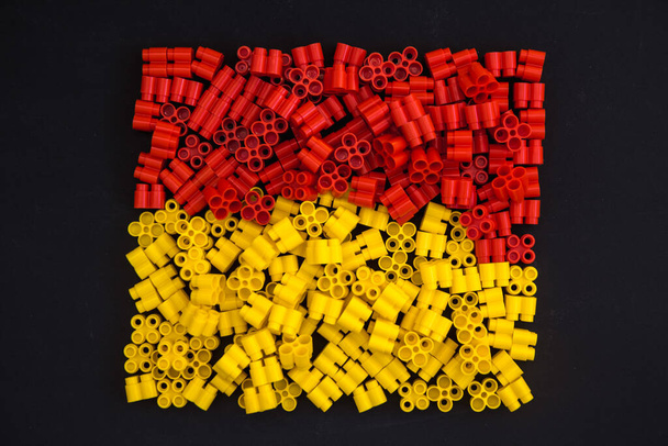 Ladrillos de plástico de color amarillo y rojo sobre fondo negro. Detalles de los juguetes. Vista superior
. - Foto, imagen