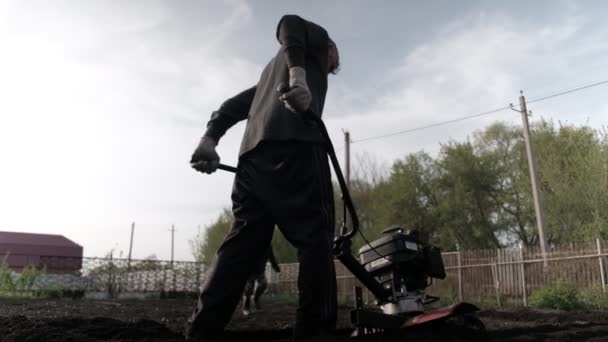 old man plowman plows the earth with a big effort motoblock. Very hard work. his wife is working a rake. 4k - Metraje, vídeo