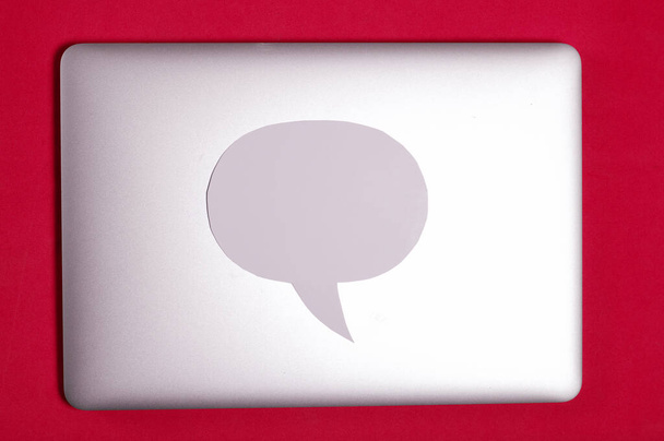 Blogger laptop with a closed lid. A speech bubble lies on the lid. Against the background of coral color. - Photo, Image