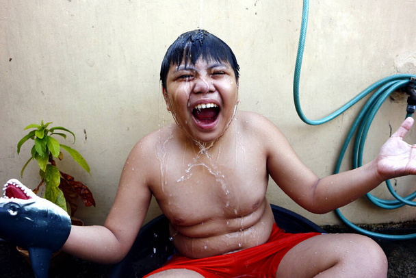 Photo of a young Asian boy cooling down in a water basin and a water hose as a makeshift shower to beat the summer heat. - Photo, image