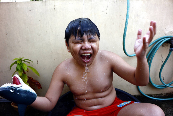 Φωτογραφία ενός νεαρού Ασιάτη που δροσίζεται σε μια λεκάνη νερού και ένα σωλήνα νερού ως πρόχειρο ντους για να νικήσει τη ζέστη του καλοκαιριού. - Φωτογραφία, εικόνα