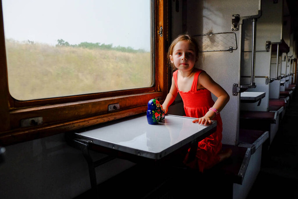 Linda chica en el tren. Concepto de vacaciones de verano y viajes. Una niña de 5 o 6 años monta en un tren. Viaja adolescente. Niña con el pelo largo. Retrato infantil
 - Foto, Imagen