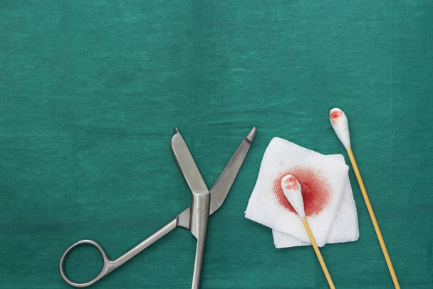 gasa, sangre, tijeras y dos bastones de algodón hisopo autobús en vestido médico quirúrgico verde con espacio para copiar
 - Foto, imagen
