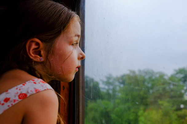 Χαριτωμένο κορίτσι στο τρένο. Καλοκαιρινές διακοπές και ταξιδιωτική ιδέα. Ένα κορίτσι 5 ή 6 ετών ταξιδεύει με τρένο. Έφηβοι ταξιδεύουν. Κοριτσάκι με μακριά μαλλιά. Παιδικό πορτρέτο - Φωτογραφία, εικόνα