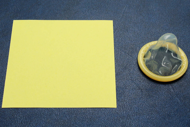 Uitgepakt condoom en blanco sticker met plaats voor een inscriptie of tekst op de achtergrond van een leren bank, afgezwakt - Foto, afbeelding