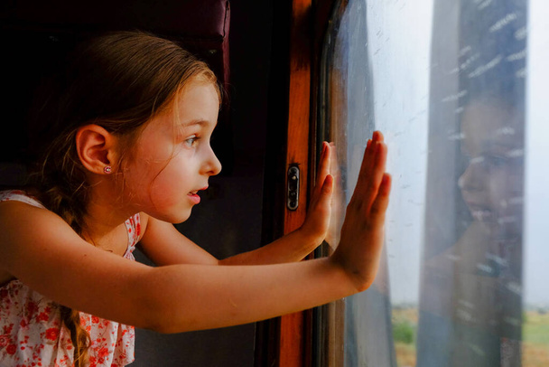 Linda chica en el tren. Concepto de vacaciones de verano y viajes. Una niña de 5 o 6 años monta en un tren. Viaja adolescente. Niña con el pelo largo. Retrato infantil
 - Foto, Imagen