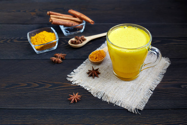 Traditionelles indisches Getränk Kurkuma-Latte oder goldene Milch mit Zimt, Sternanis und Kurkuma auf einem rustikalen Holztisch. - Foto, Bild