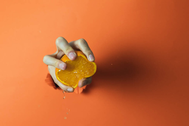 Hand holding and squeezing an orange. Orange background - Фото, изображение