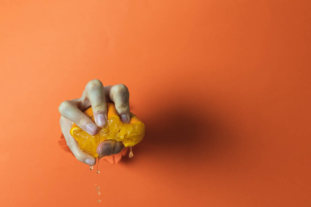 Рука держит и сжимает апельсин. Оранжевый фон
 - Фото, изображение
