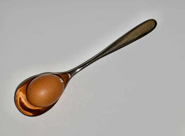 Grande cuillère à soupe d'argent tenant un œuf brun sur fond blanc
 - Photo, image