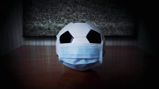 The ball in the medical mask near the idle TV. Football match canceled. World epidemic. Cancel mass events. Cancel, reschedule football championship. Coronavirus. TV without image. Upset fans. Glitch - Footage, Video
