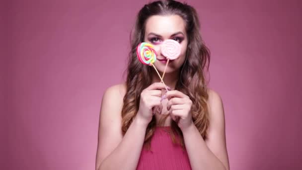 Jonge sexy vrouw die lolly eet. Studio shoot op roze achtergrond. - Video