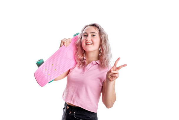 A blonde girl with curly hair in a pink t-shirt. Happy young lady with a pink skateboard. Isolated on a white background - Fotoğraf, Görsel