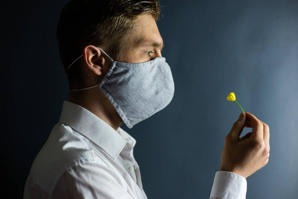 Ο άντρας με τη μάσκα "Σταματήστε τον ιό του Coronavirus" μυρίζει φρέσκο λουλούδι, COVID-19. - Φωτογραφία, εικόνα