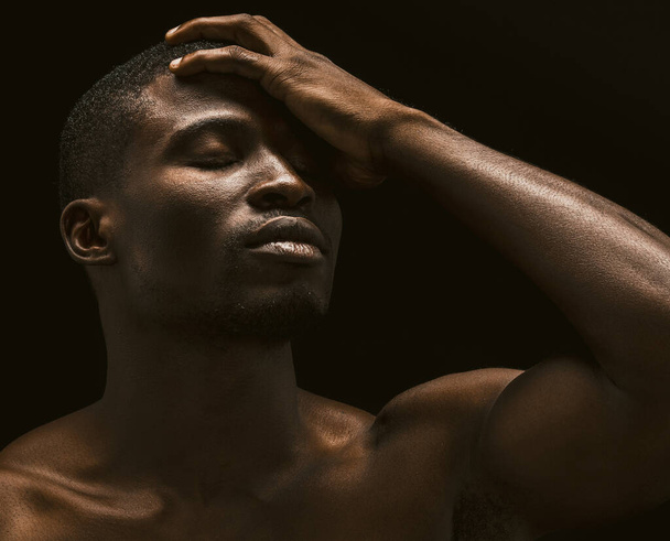 Sexy Afro-Amerikaanse man toont gezicht palm gebaar. portret van een naakte man met gesloten ogen op zwarte achtergrond die zijn gezicht bedekt met zijn hand - Foto, afbeelding