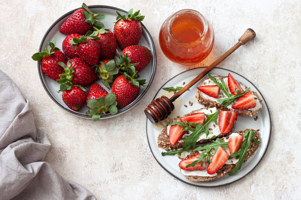 El desayuno sabroso - el bocadillo con el queso de crema, las fresas y la rúcula
 - Foto, imagen